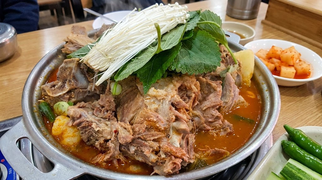 A steaming pot of Korean Hangover Soup Haejang-guk, specifically Gamjatang (pork back-bone stew) with mushrooms and perilla leaves.